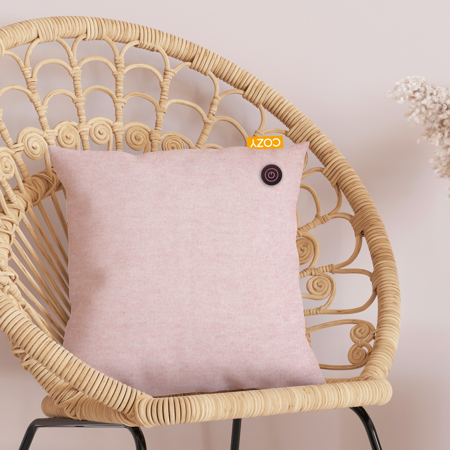 Coussin de massage Cozy rose sur une chaise en osier avec étiquette orange et bouton.