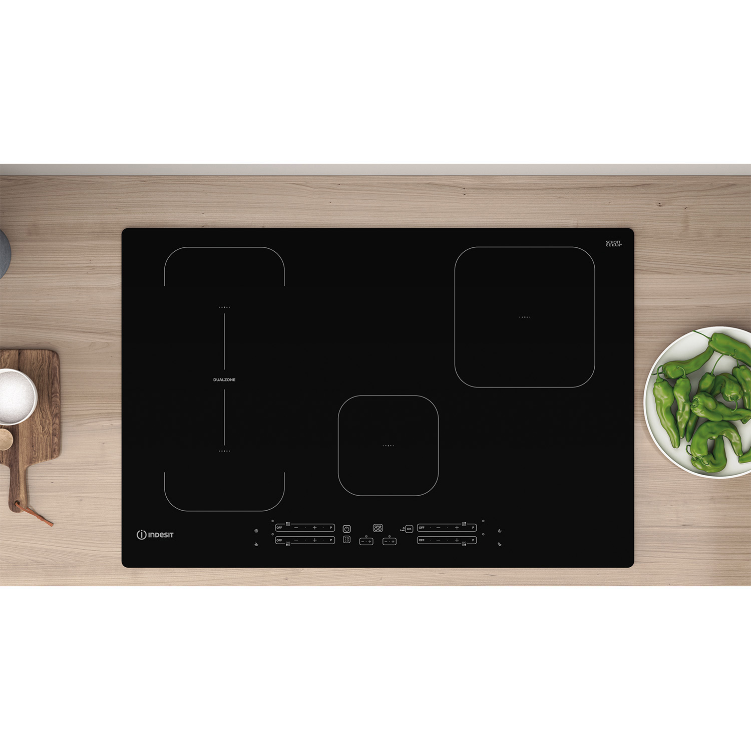 Piano cottura a induzione nero con quattro fuochi. Un tagliere in legno e peperoni verdi accanto.