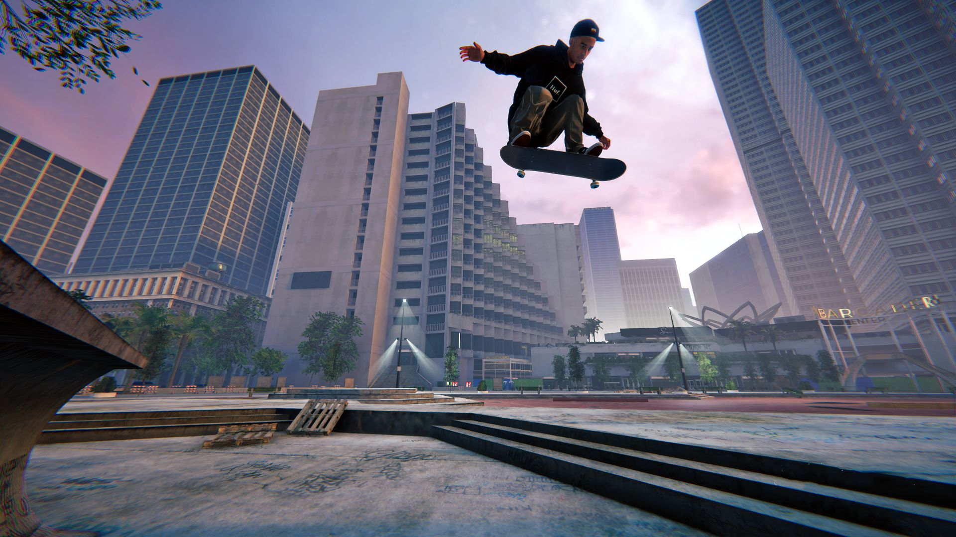 Un skateur est en l'air, effectuant une figure dans une ville. Bâtiments et un parc en arrière-plan.