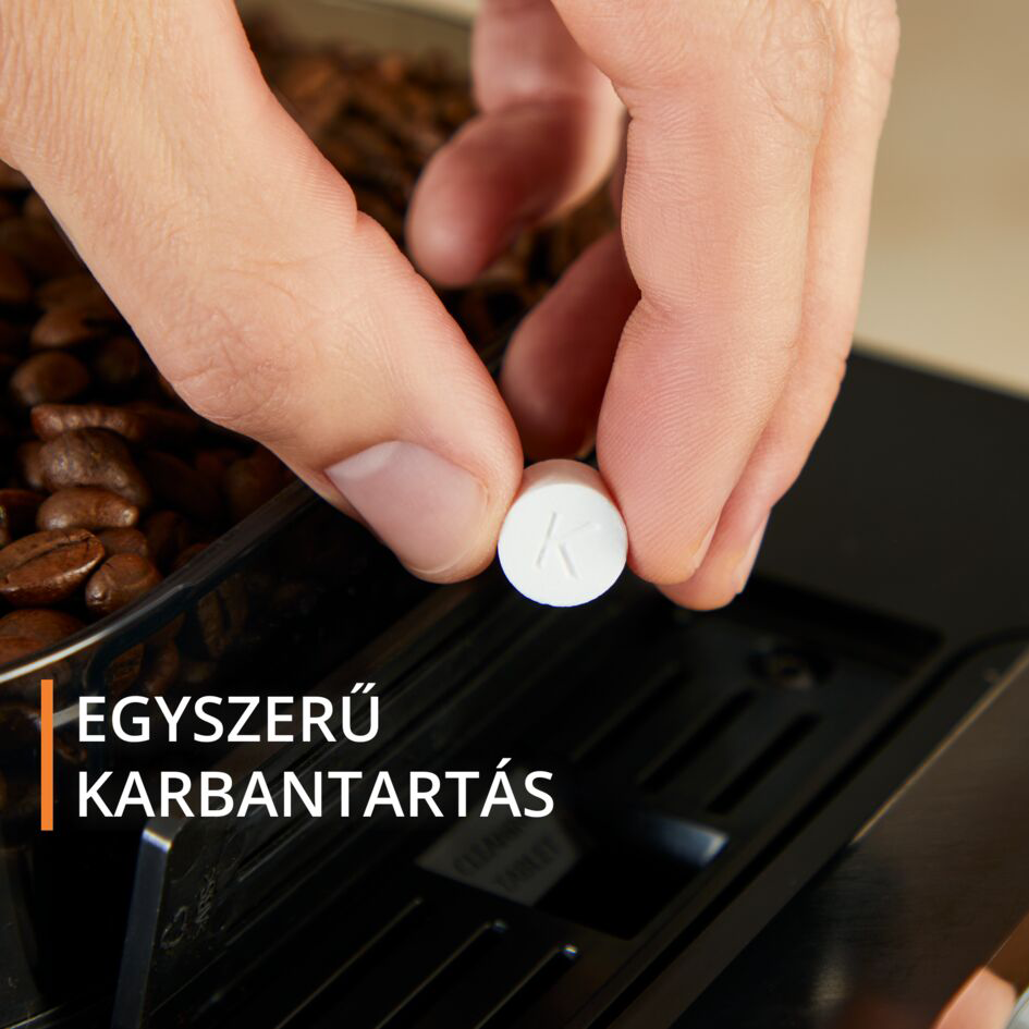 Egy személy keze egy fehér tablettát tart, kávébabok mellett.