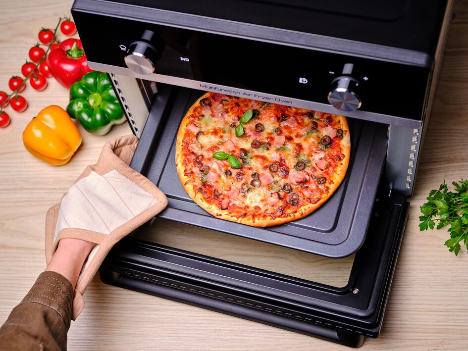 A pizzát egy fekete fritőz sütőből veszik ki sütőkesztyűvel.