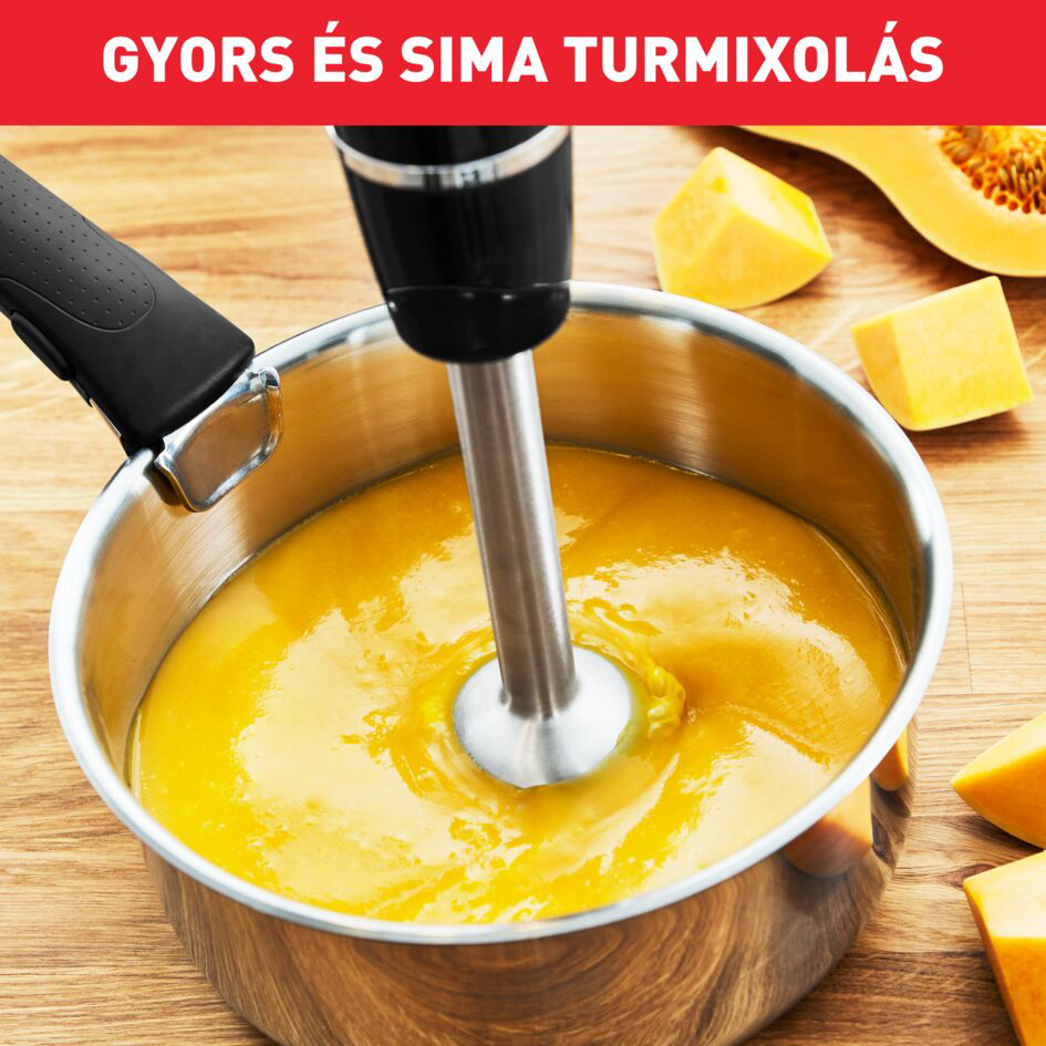 Egy botmixer egy sárga leveses fazékban, tökfélék darabjaival körülvéve.