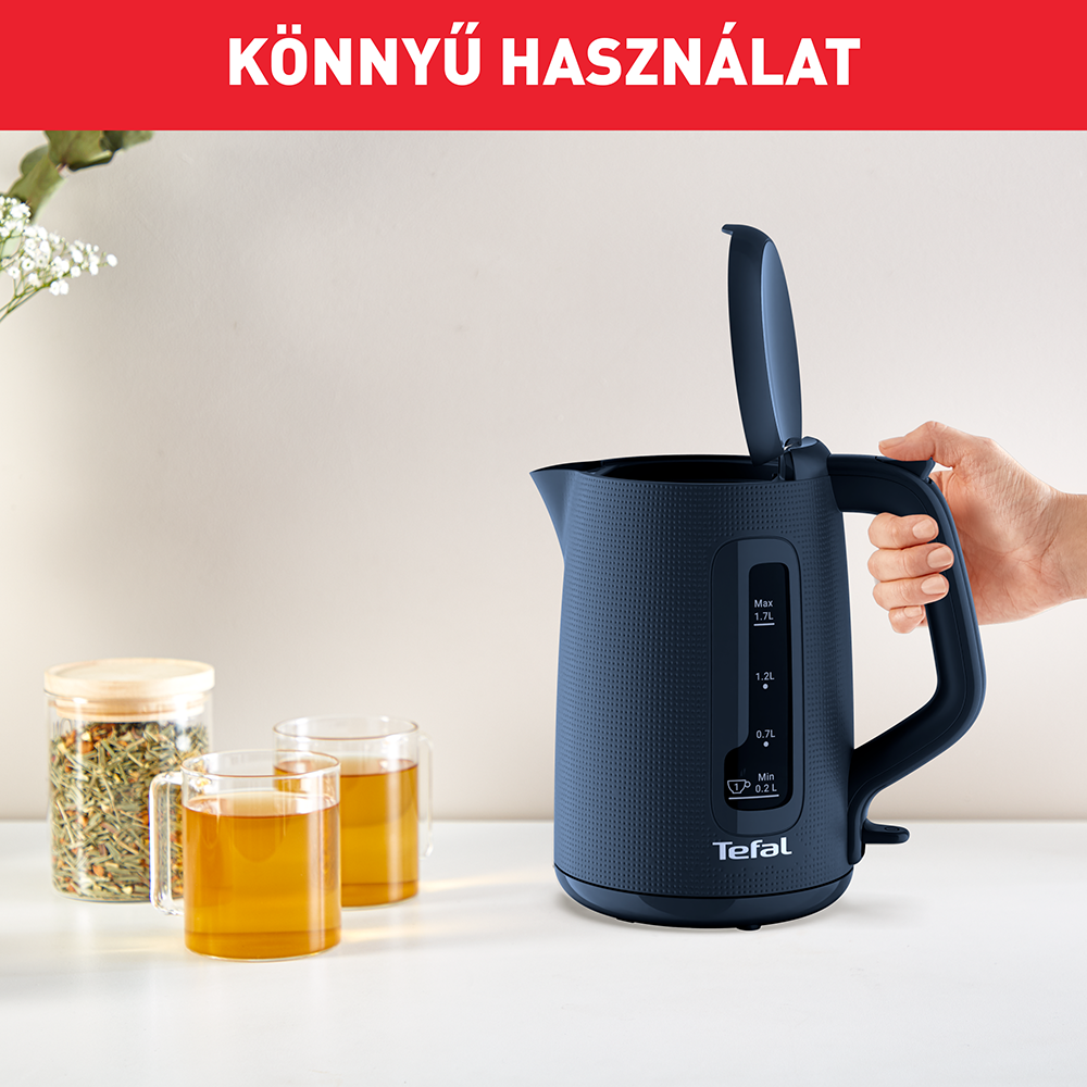 Egy kék vízforraló nyitott fedéllel, tea és virágcsokrok mellett, otthoni környezetben.