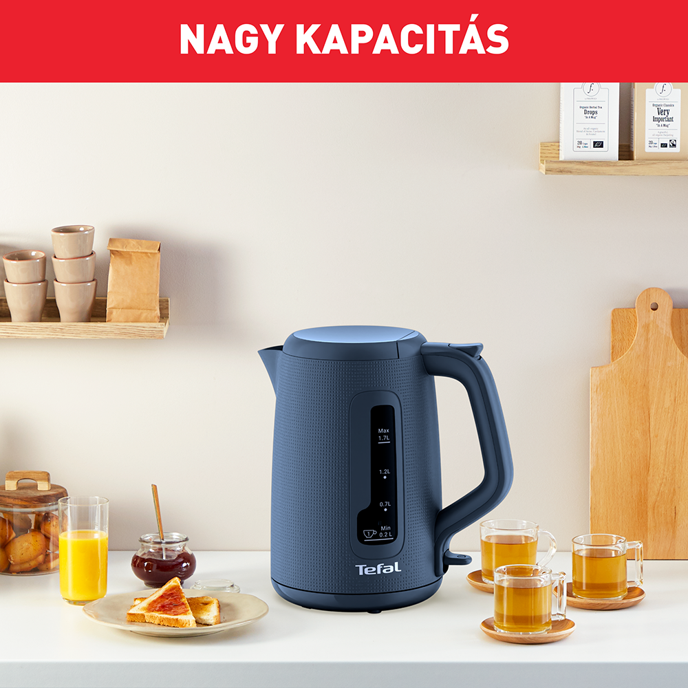 Kék vízforraló fogantyúval, teáscsészékkel és lekvárral fehér felületen, 'Nagy Kapacitás' szóval.