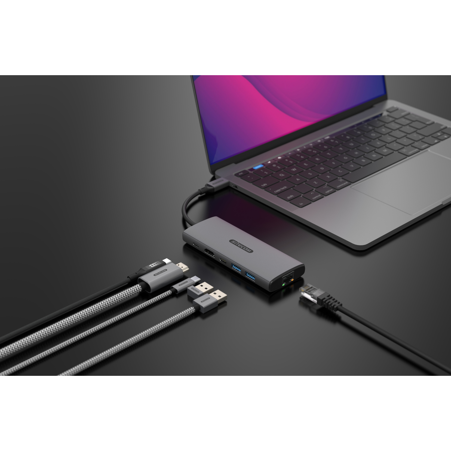 A gray hub connected to a laptop with various cables on a dark surface.