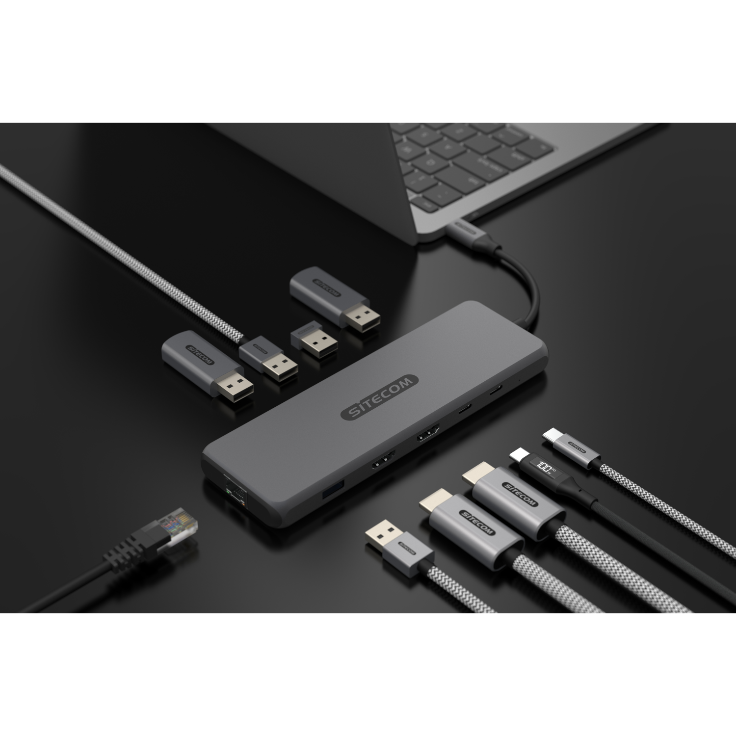 A gray hub with multiple ports, connected to a laptop. Cables and adapters are scattered around the hub.