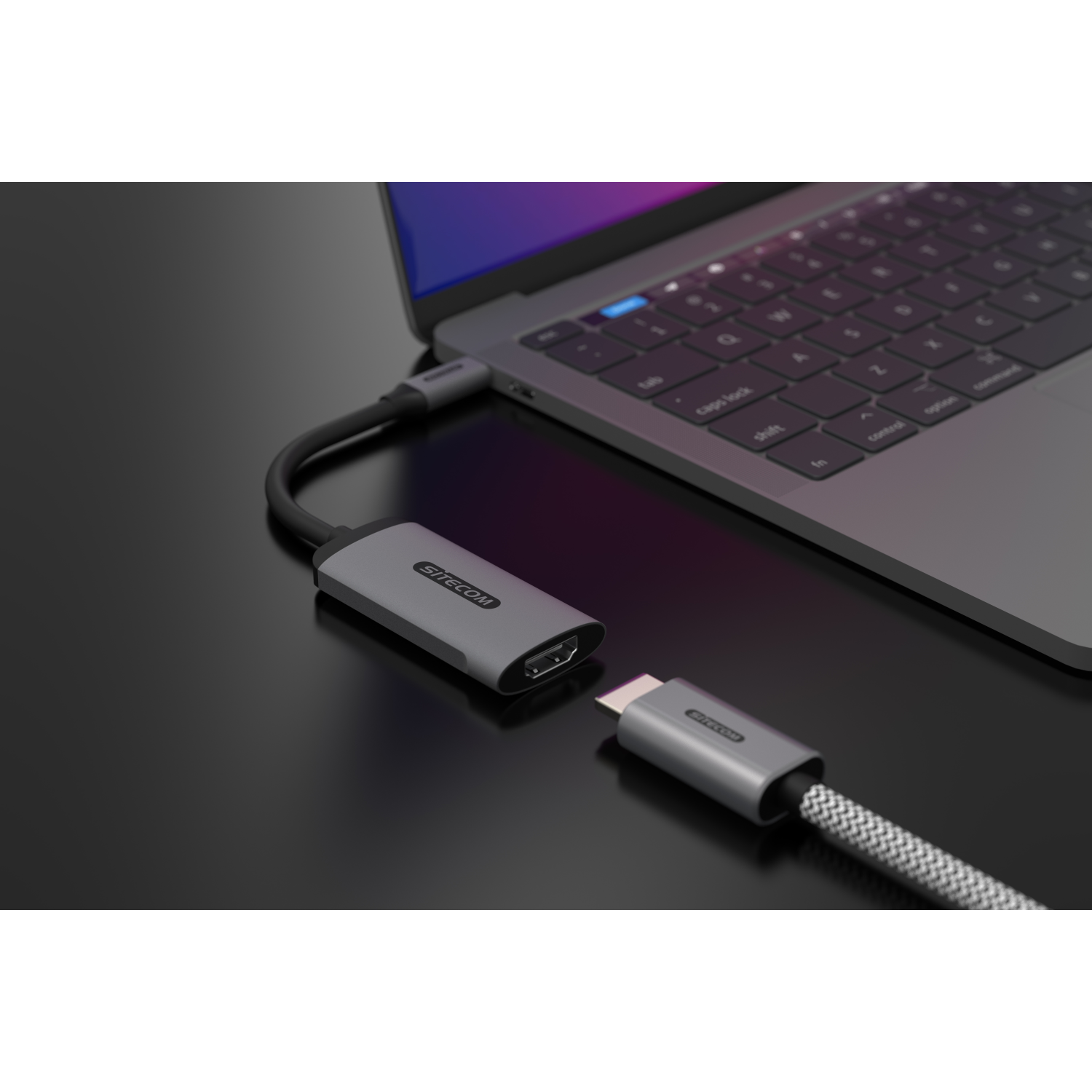 Een grijze HDMI-adapter aangesloten op een laptop. Een USB-C-connector is aangesloten op de adapter.