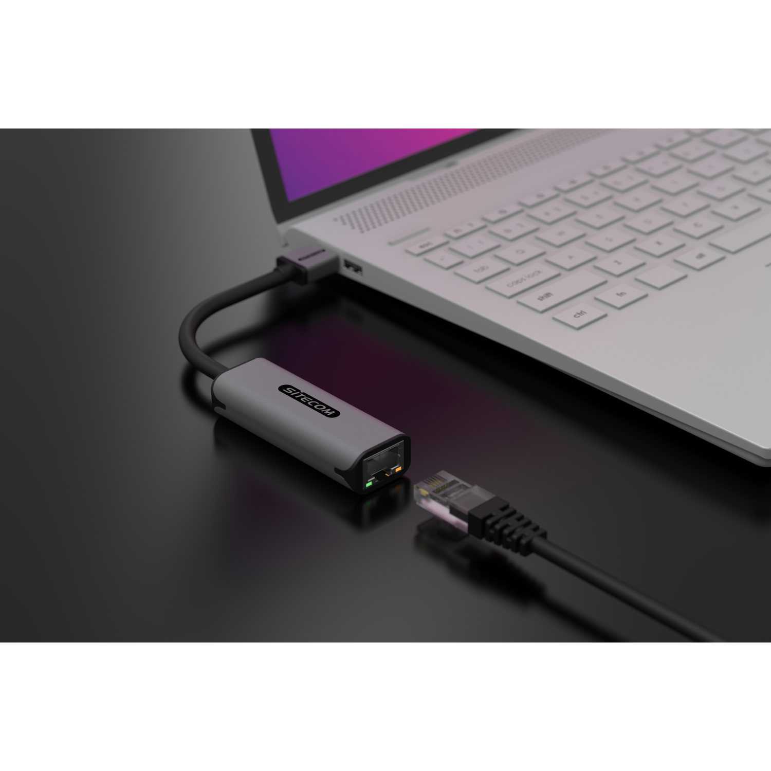 A black Sitcom adapter connected to a laptop via a cable, another cable plugged into it.