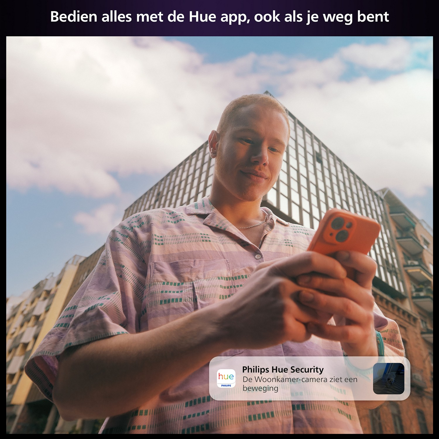 Een man met een oranje telefoon gebruikt de Hue-app. Gebouwen en blauwe lucht zijn zichtbaar.