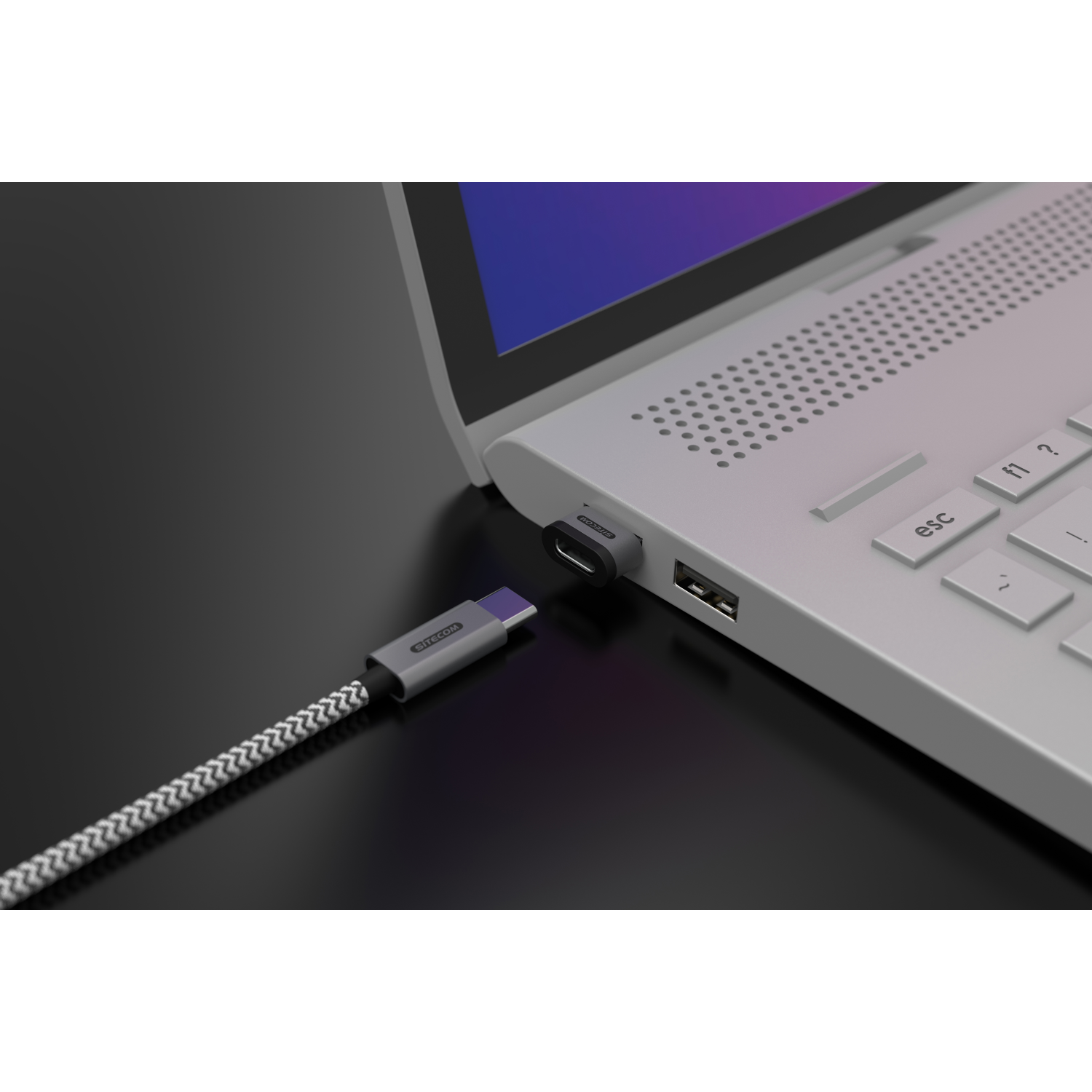 Laptop connected to a USB-C cable and adapter, on a black surface.