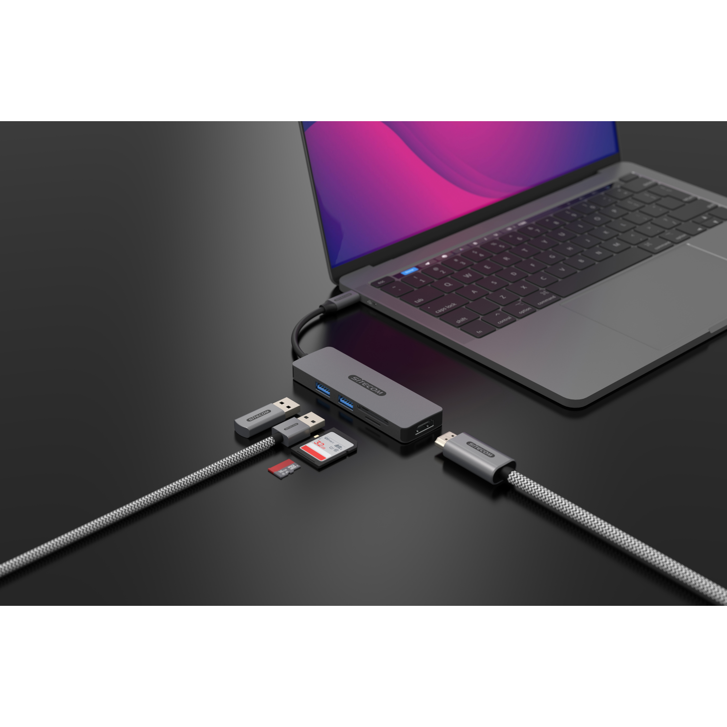 Laptop connected to a hub with USB, SD card, and HDMI connectors. All on a dark surface.