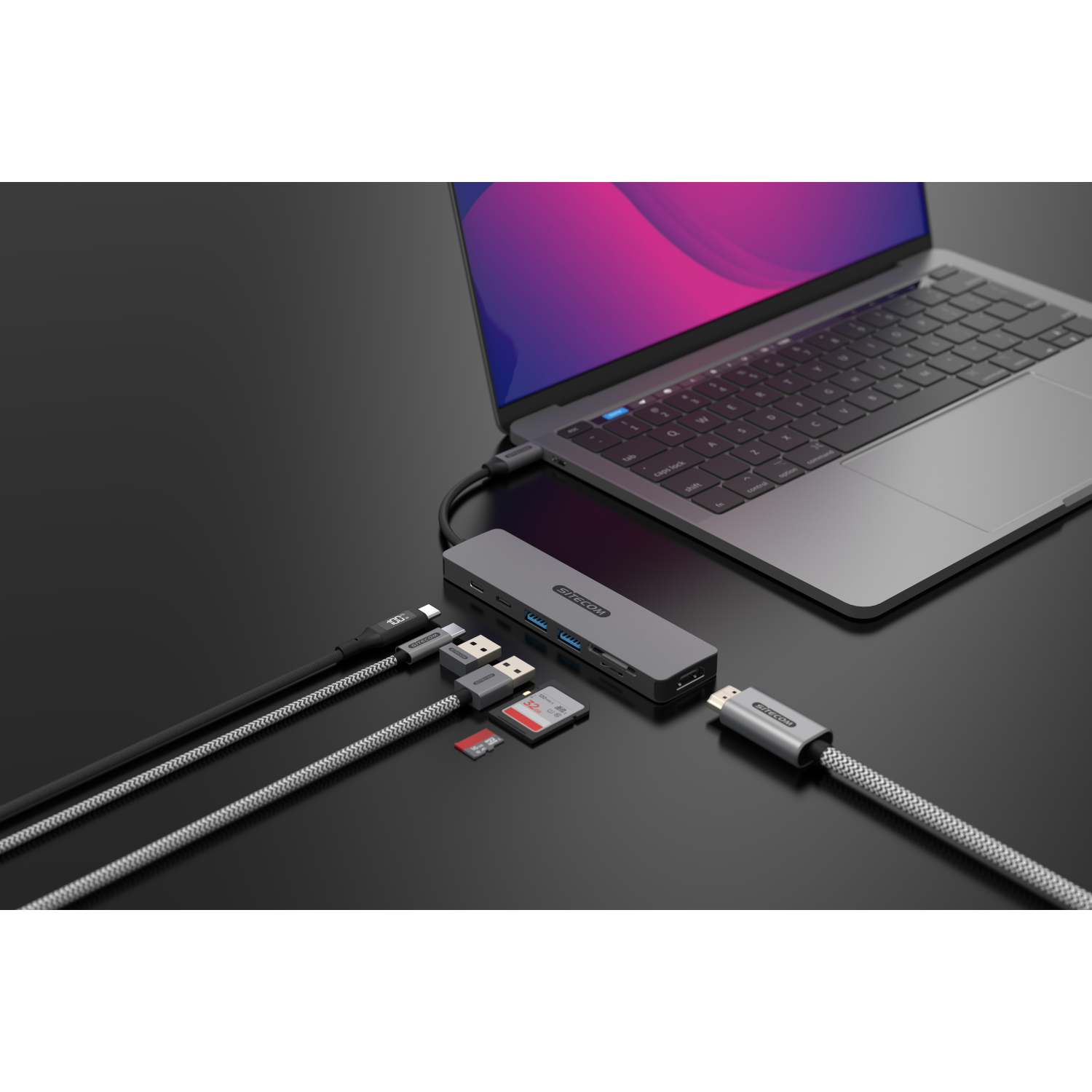 A laptop connected to a hub with multiple cables and devices, on a dark surface.