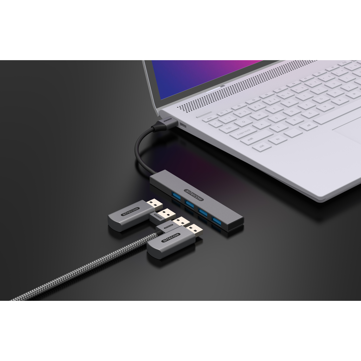 A laptop connected to a USB hub with two adapters. Black background.