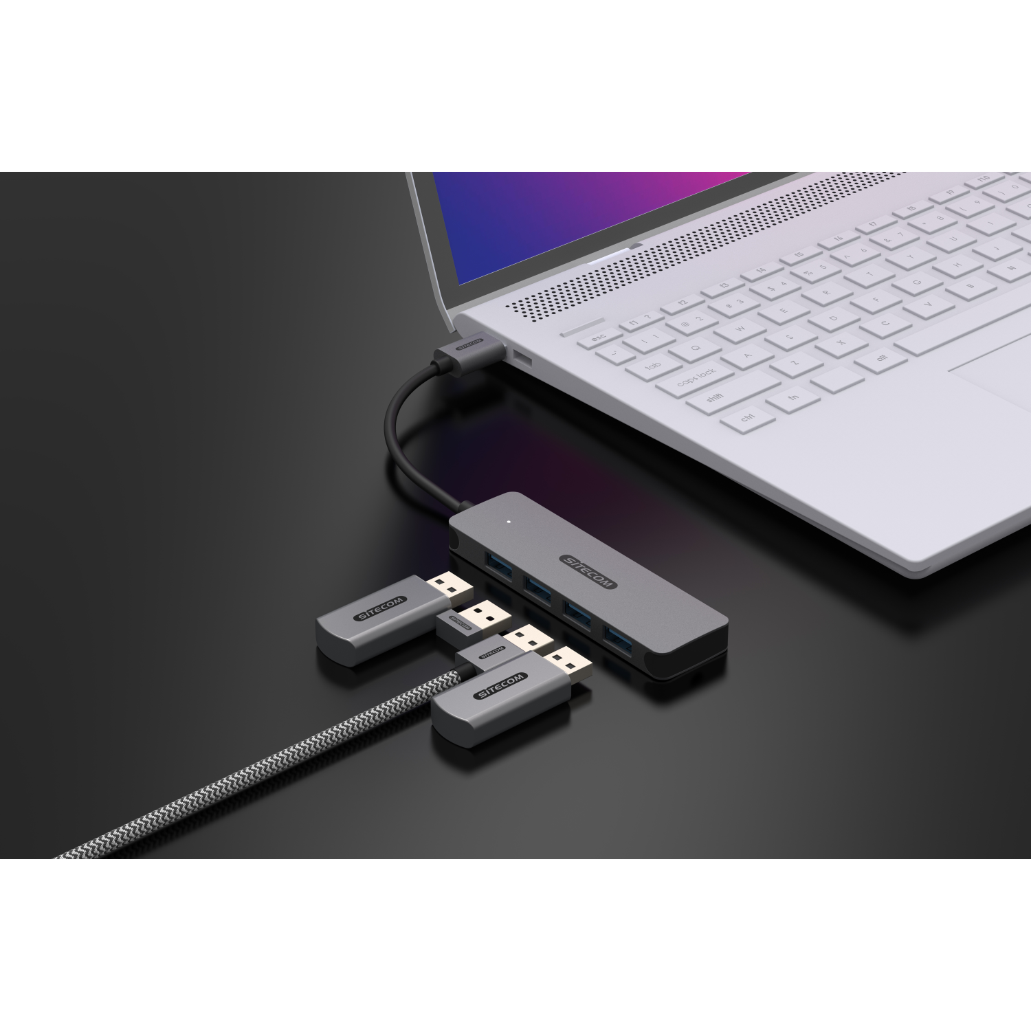 A laptop connected to a hub, with USB drives attached, on a dark surface.