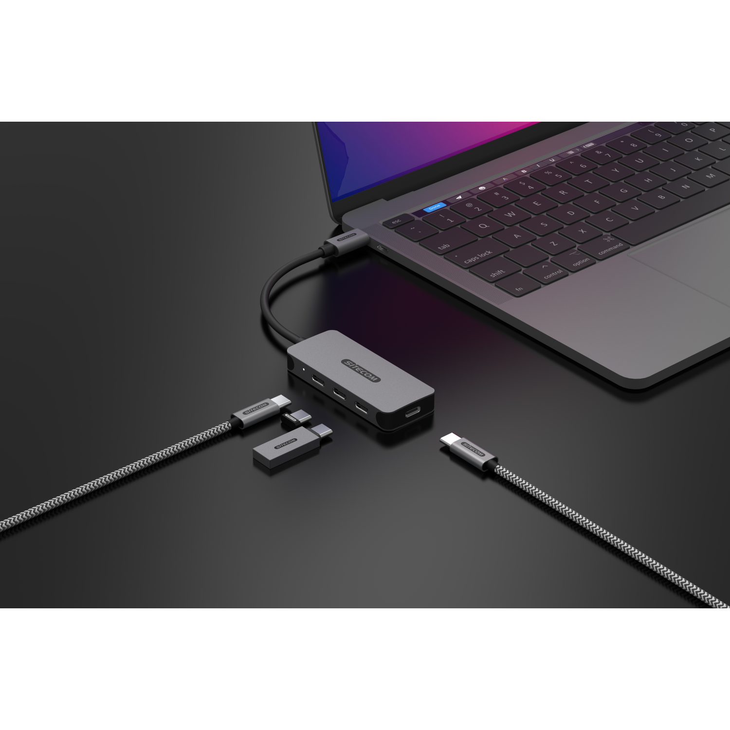 Laptop with a hub connected, and cables and adapters on a black surface.