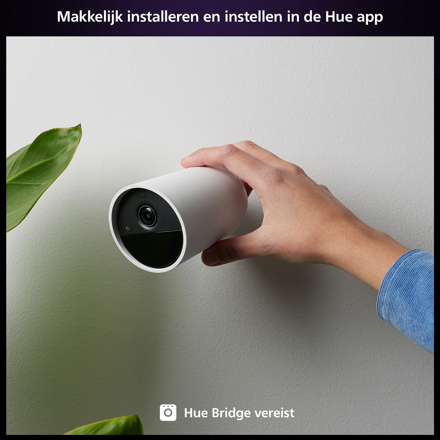 Een hand die een witte beveiligingscamera vasthoudt, aan een muur gemonteerd, met de tekst 'Hue Bridge vereist'.