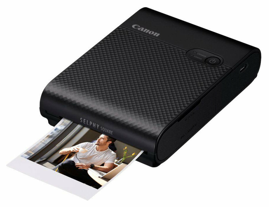 Czarna drukarka Canon Selphy Square drukująca zdjęcie. Na zdjęciu mężczyzna w pomieszczeniu.