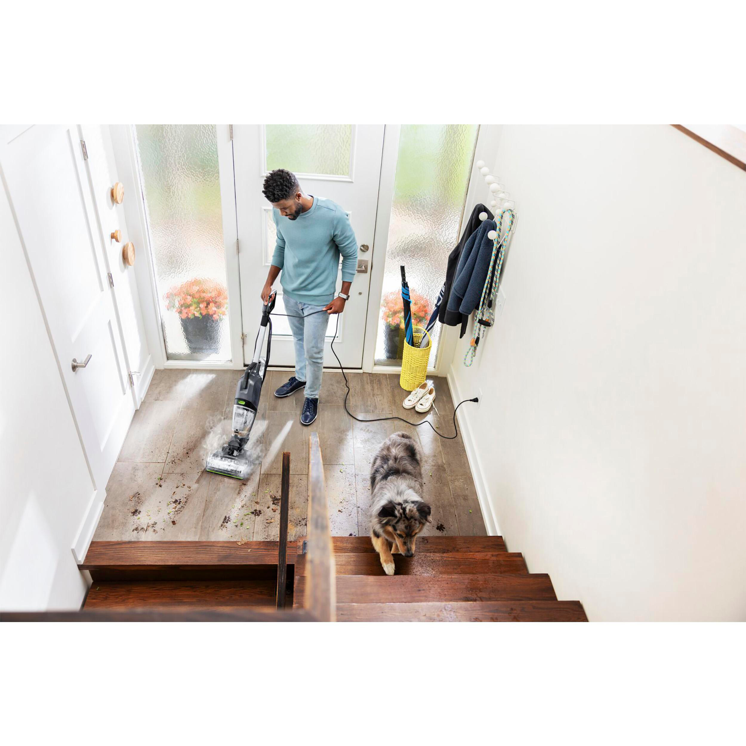 Ein Mann saugt einen Holzboden ab, ein Hund ist in der Nähe. Der Boden ist schmutzig.