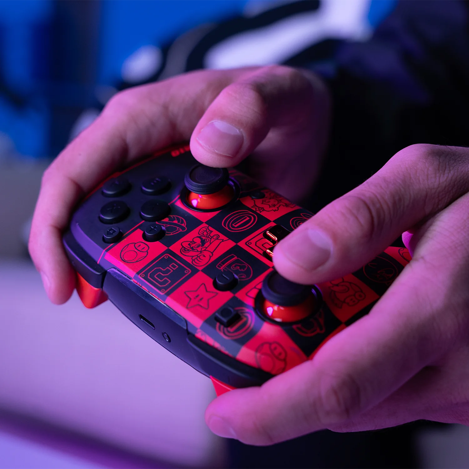Mani che tengono un controller di gioco a tema Mario rosso. Pulsanti neri e cappucci joystick rossi.