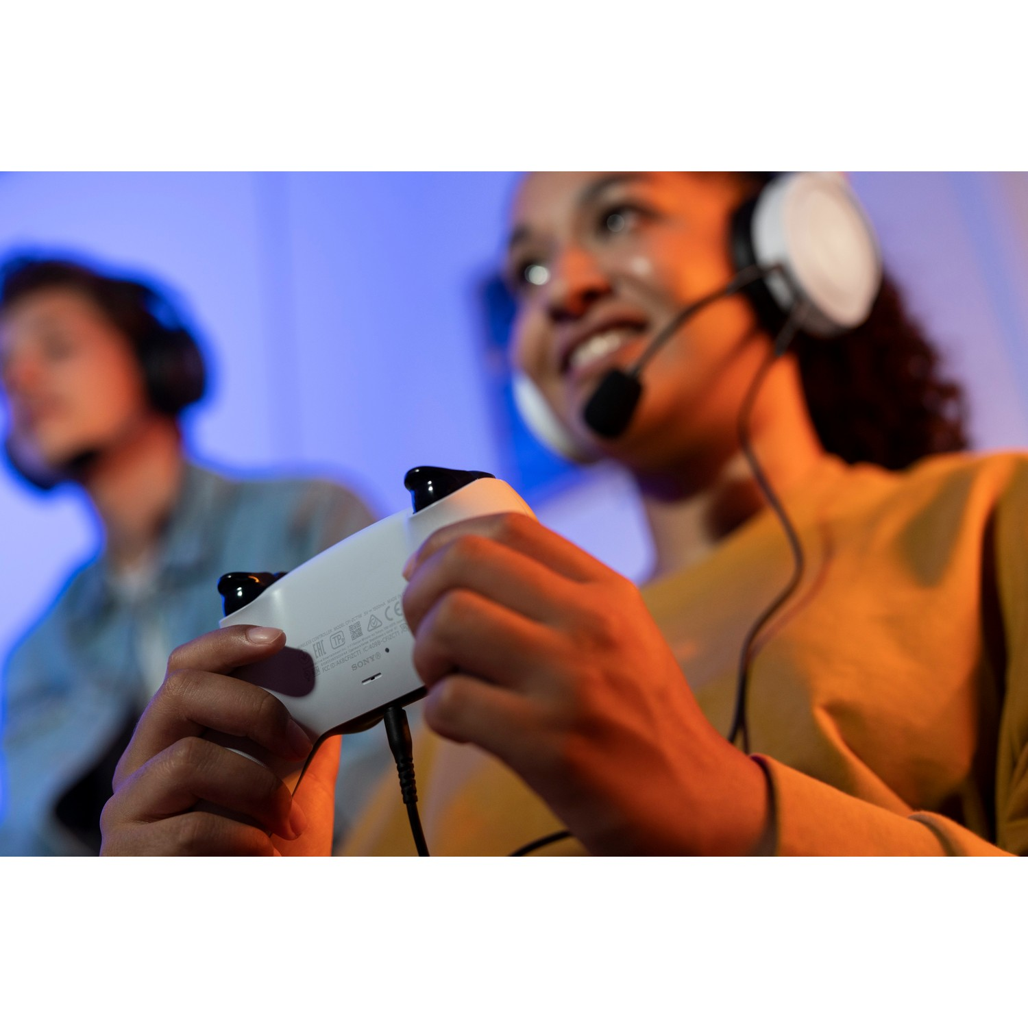 Two people gaming, one wearing a headset and holding a white controller.