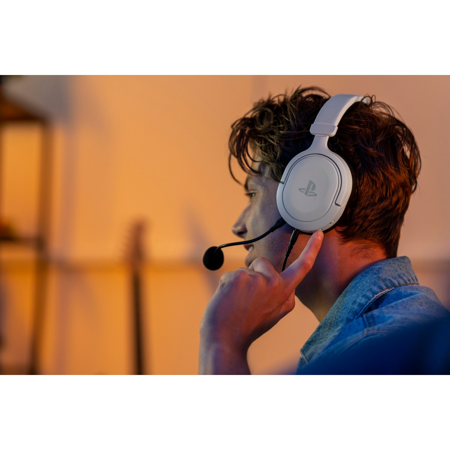 Man wearing white gaming headset, looking right, in a room with orange lighting.