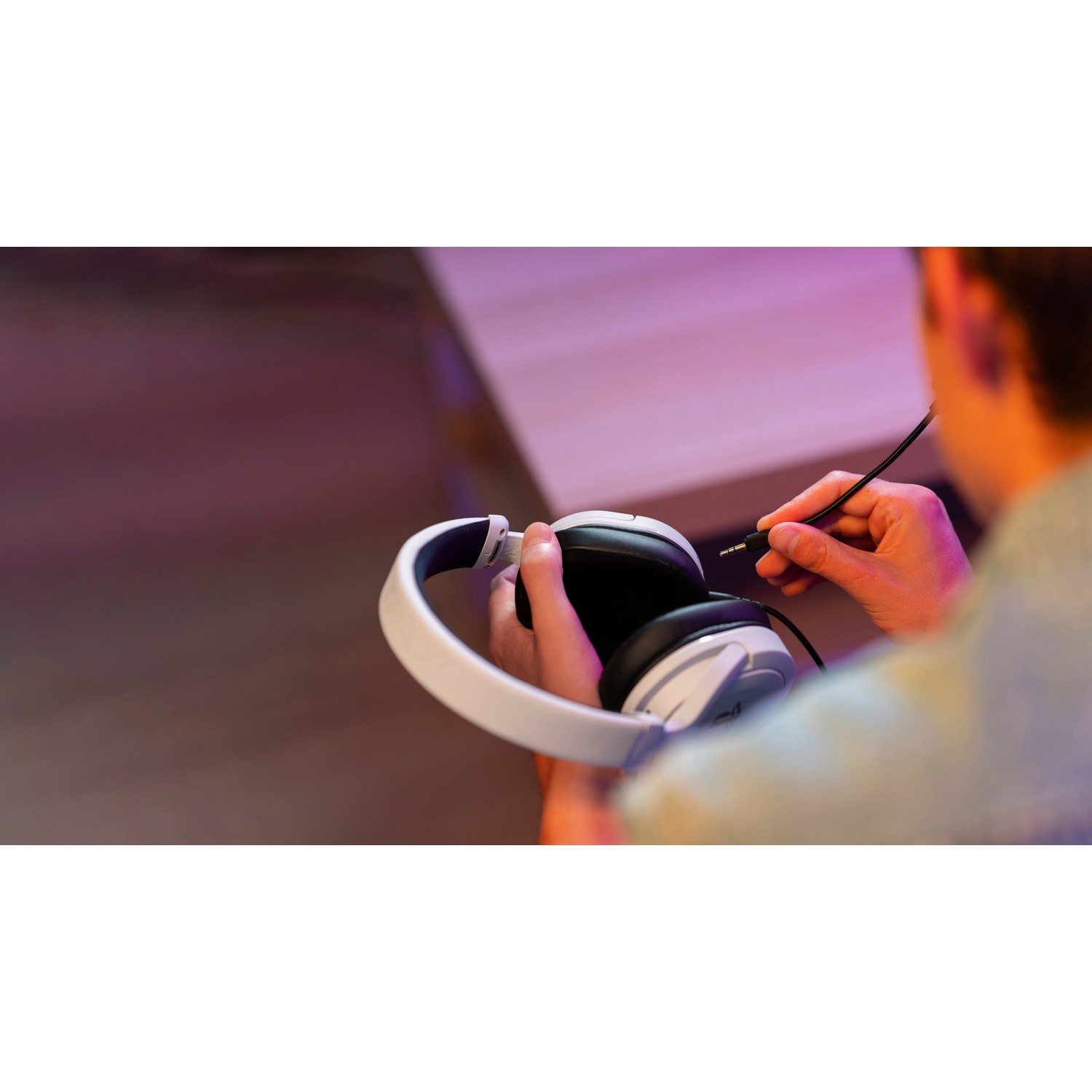 A person holding a white headphone and connecting a black cable.