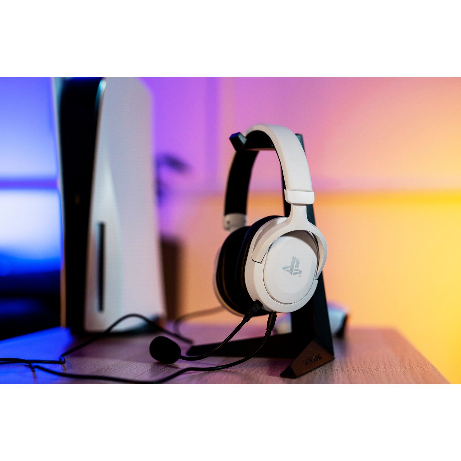 White gaming headset on a black stand. PlayStation 5 console in the background.