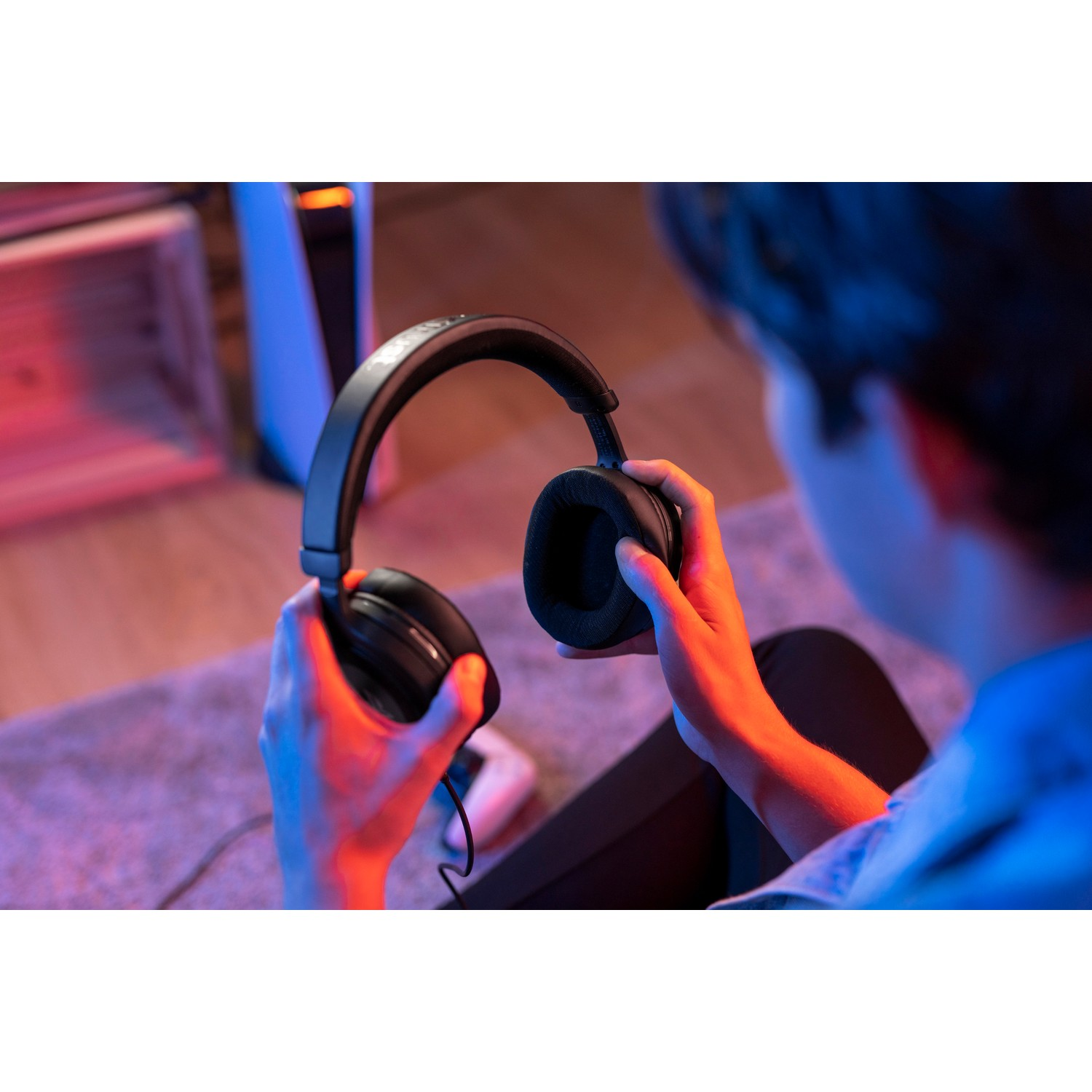 A person holding a black gaming headset in their hands.