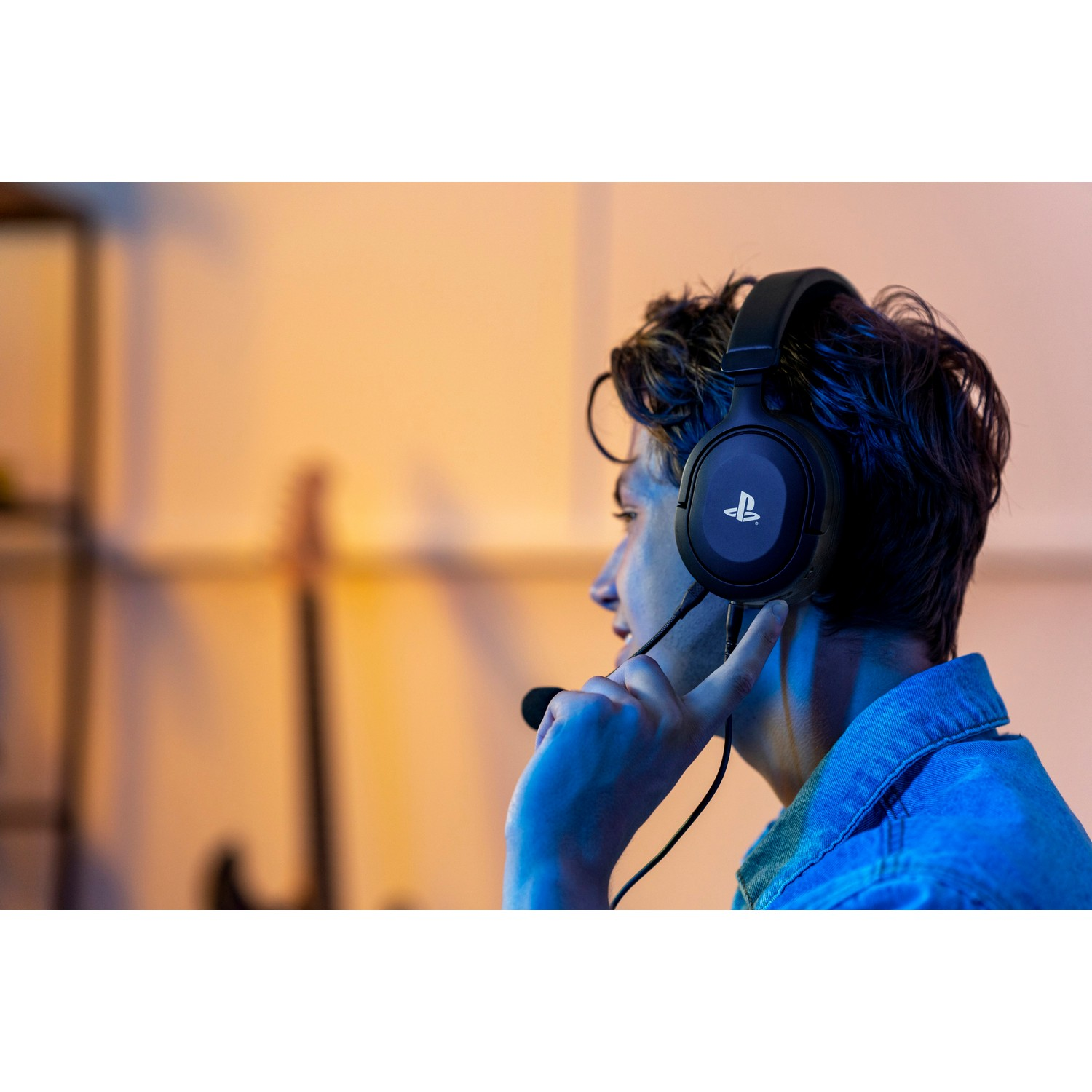 Man wearing a headset, looking to the left. A guitar is in the background.