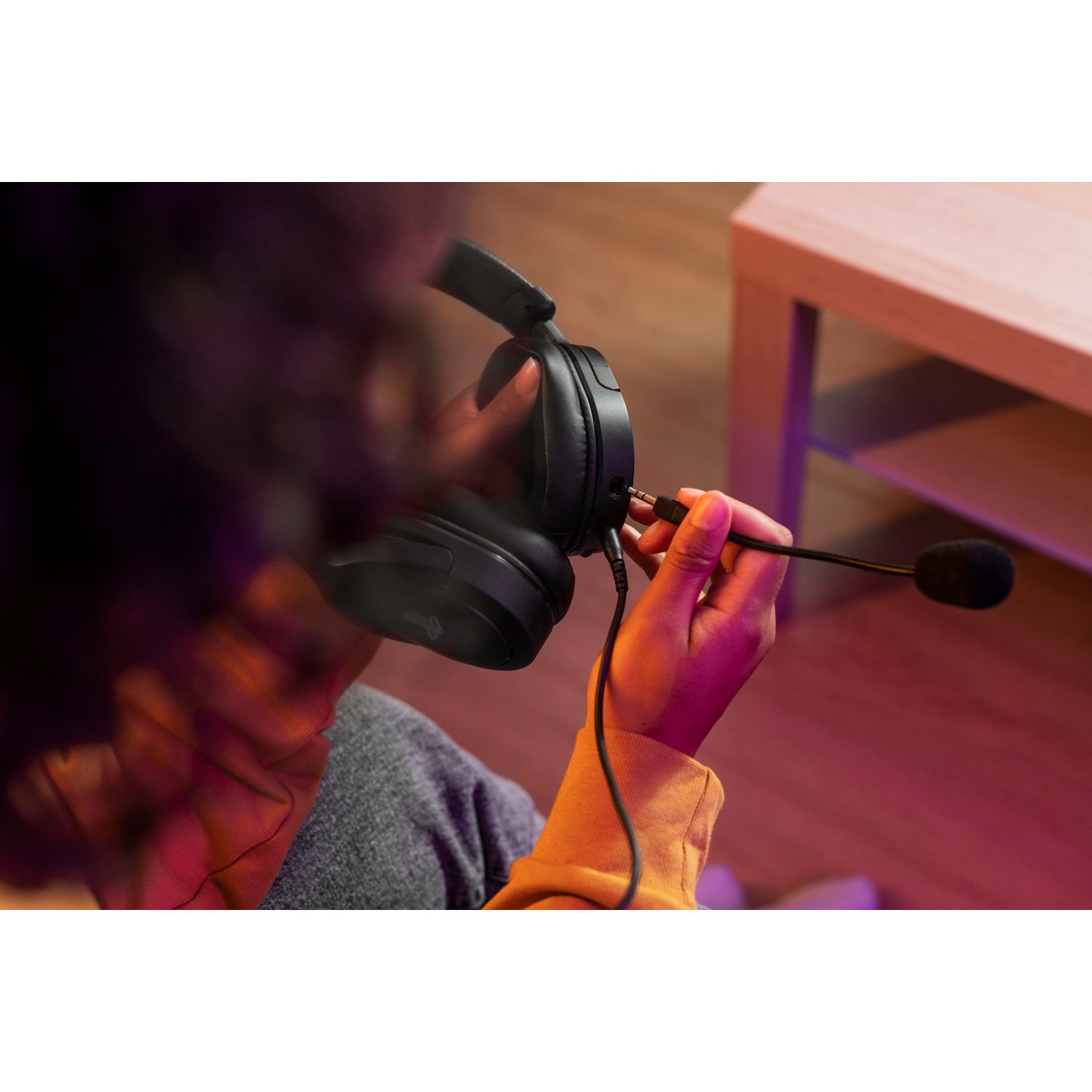 Person plugging in a headset. The headset is black, and the background is blurry.