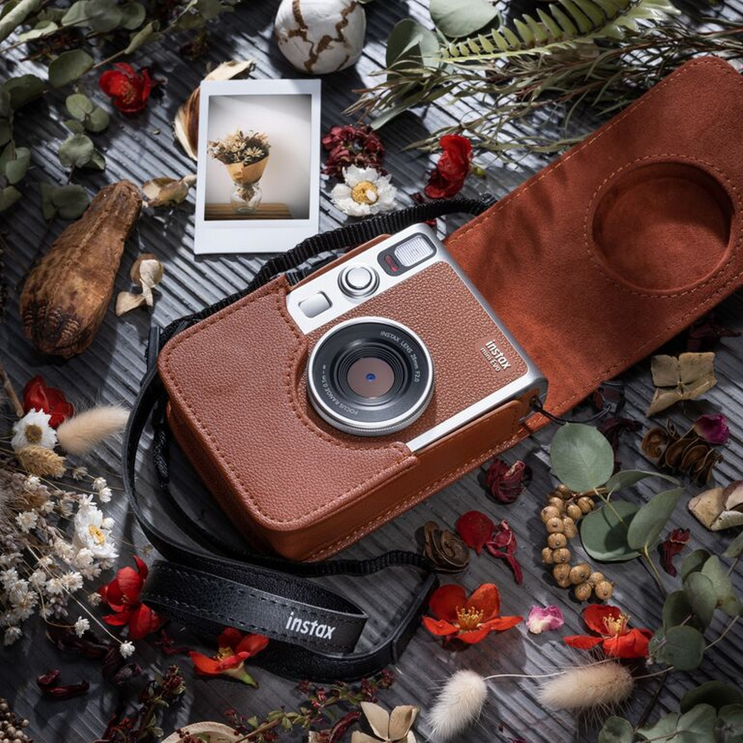 Brown leather camera in a case. Dried flowers and other items surround it.