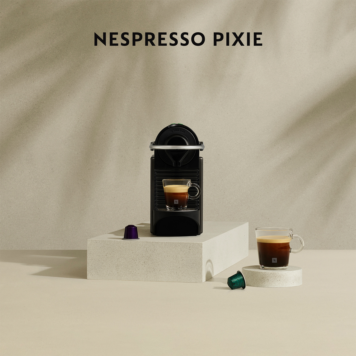 Macchina da caffè Nespresso Pixie nera con una tazza di caffè. Si vedono una capsula e una tazza.