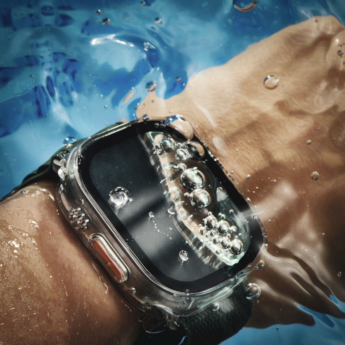 Das Handgelenk einer Person mit einer Smartwatch in einem transparenten Gehäuse, das in blaues Wasser getaucht ist.