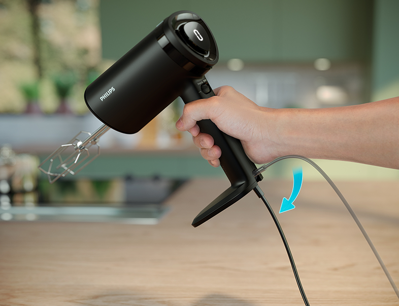 Fekete Philips kézi mixer kézben, töltőkábel csatlakoztatva, fa felületen.