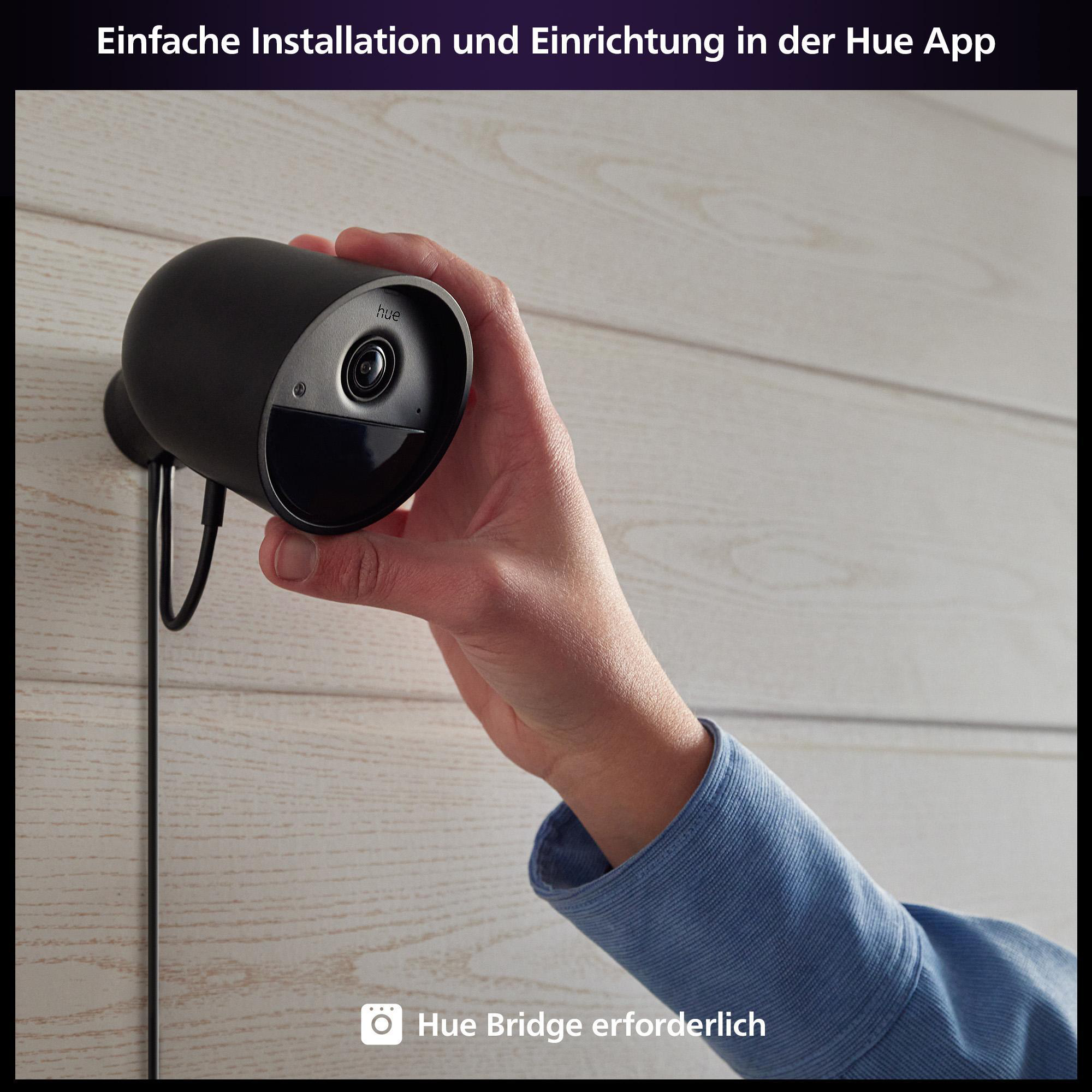 Eine Person installiert eine schwarze Hue-Sicherheitskamera an einer Holzwand.