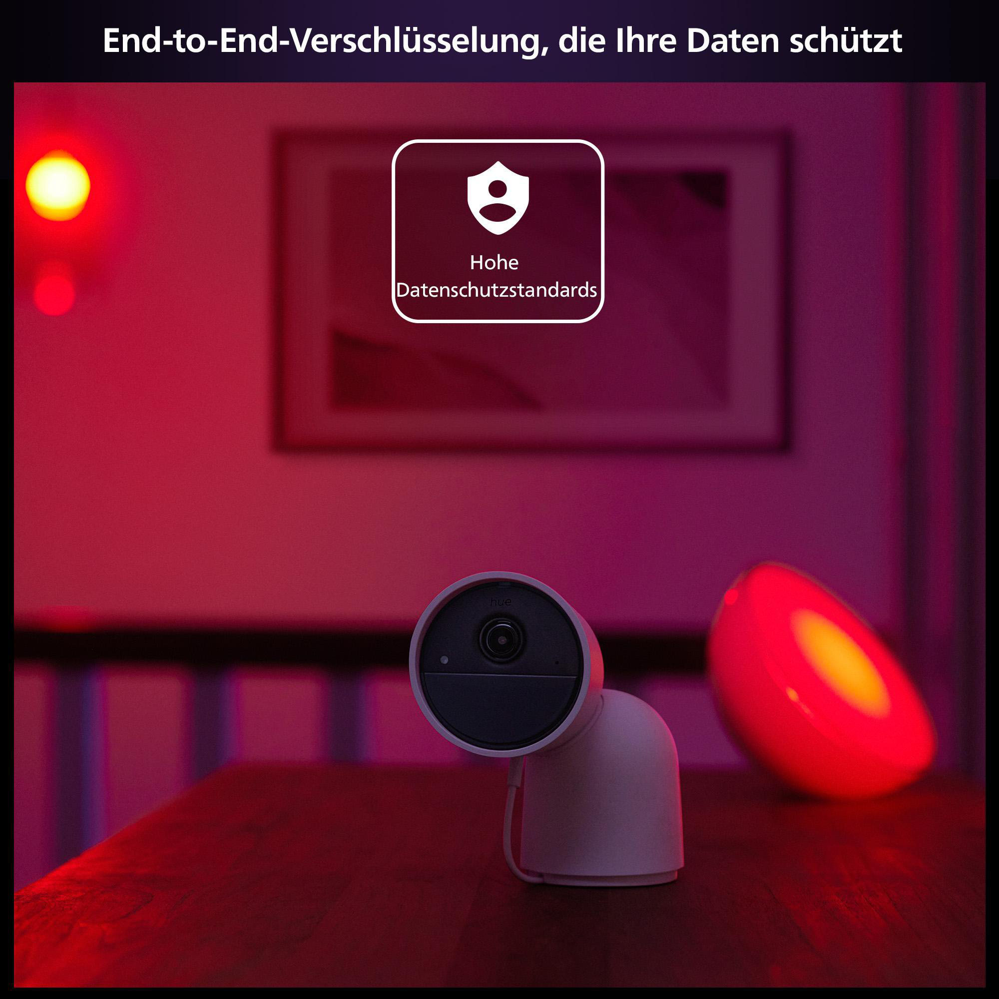 Weiße Überwachungskamera auf einem Tisch, mit rotem Licht und einem Bild im Hintergrund.