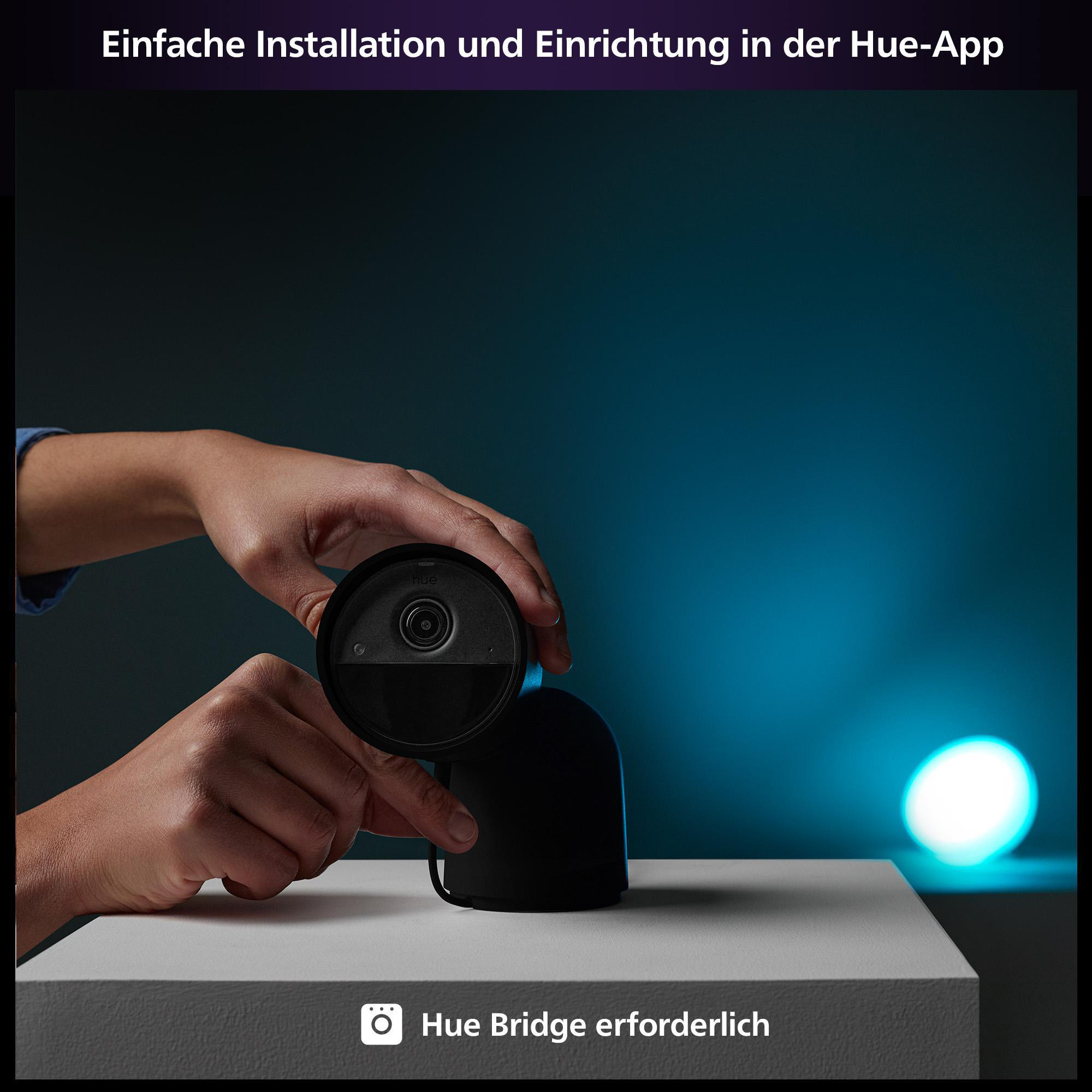 Hände halten eine schwarze Smart-Home-Kamera auf einer weißen Oberfläche, blaue Beleuchtung.