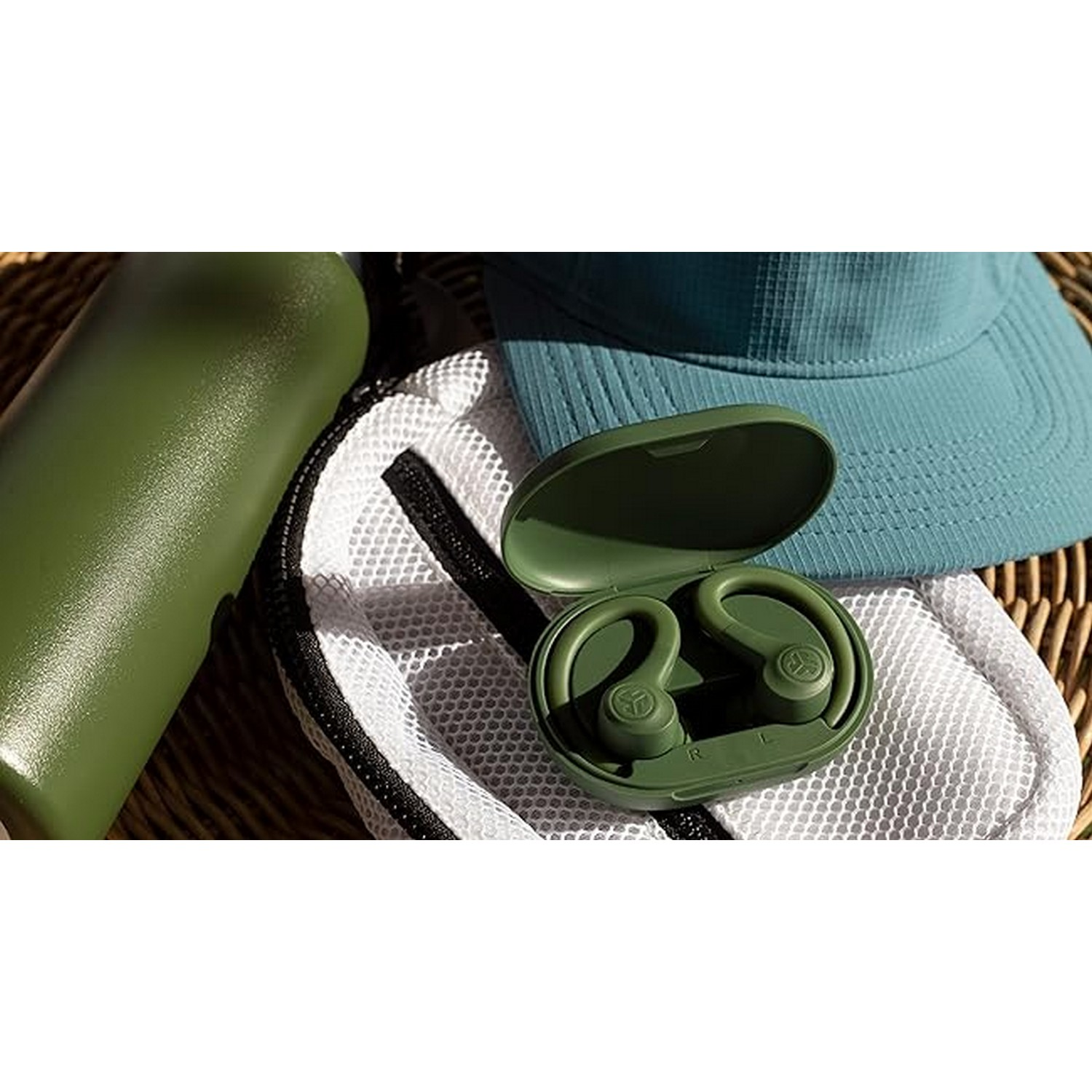 Green wireless earbuds in a case. A green water bottle and a cap are also visible. Outdoors setup.