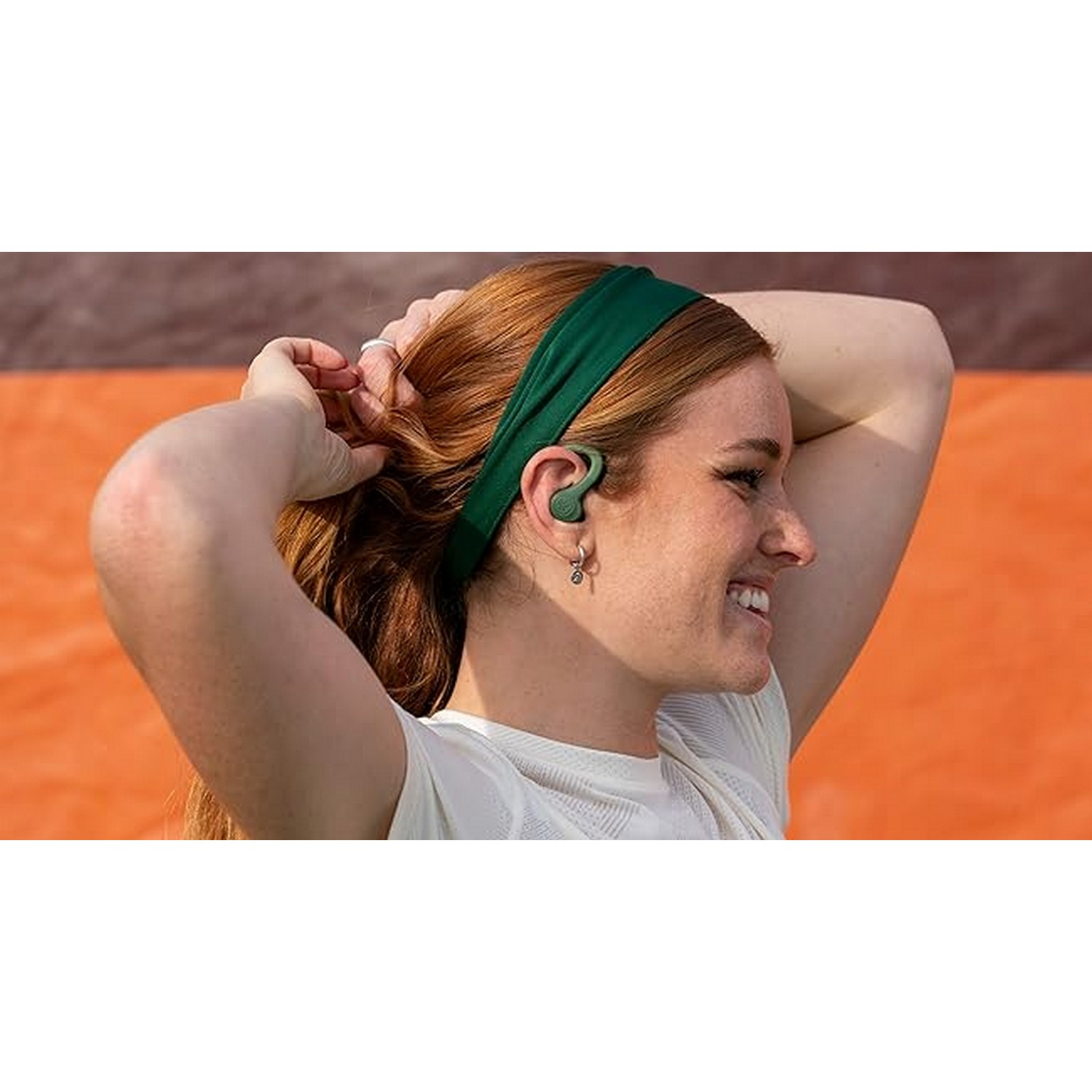 Woman with green headband and earbud, smiling. Shows profile.