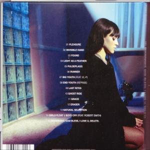 Egy sötét hajú nő egy üvegtömb fal mellett áll, és a CD hátulját nézi, a számok neveivel.