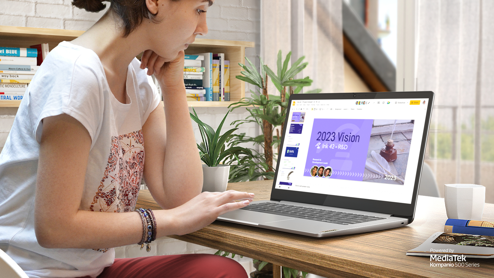 Eine Frau arbeitet an einem Laptop mit einer Präsentation. Bücher stehen im Regal hinter ihr. Der Laptop ist geöffnet.