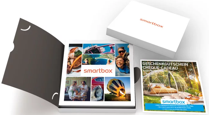 Une boîte cadeau Smartbox, ouverte, montrant diverses images. Une brochure est sur le côté.