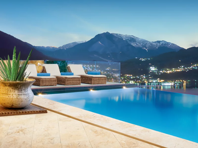 Piscina a sfioro al crepuscolo, con vista sulle montagne e le luci della città.