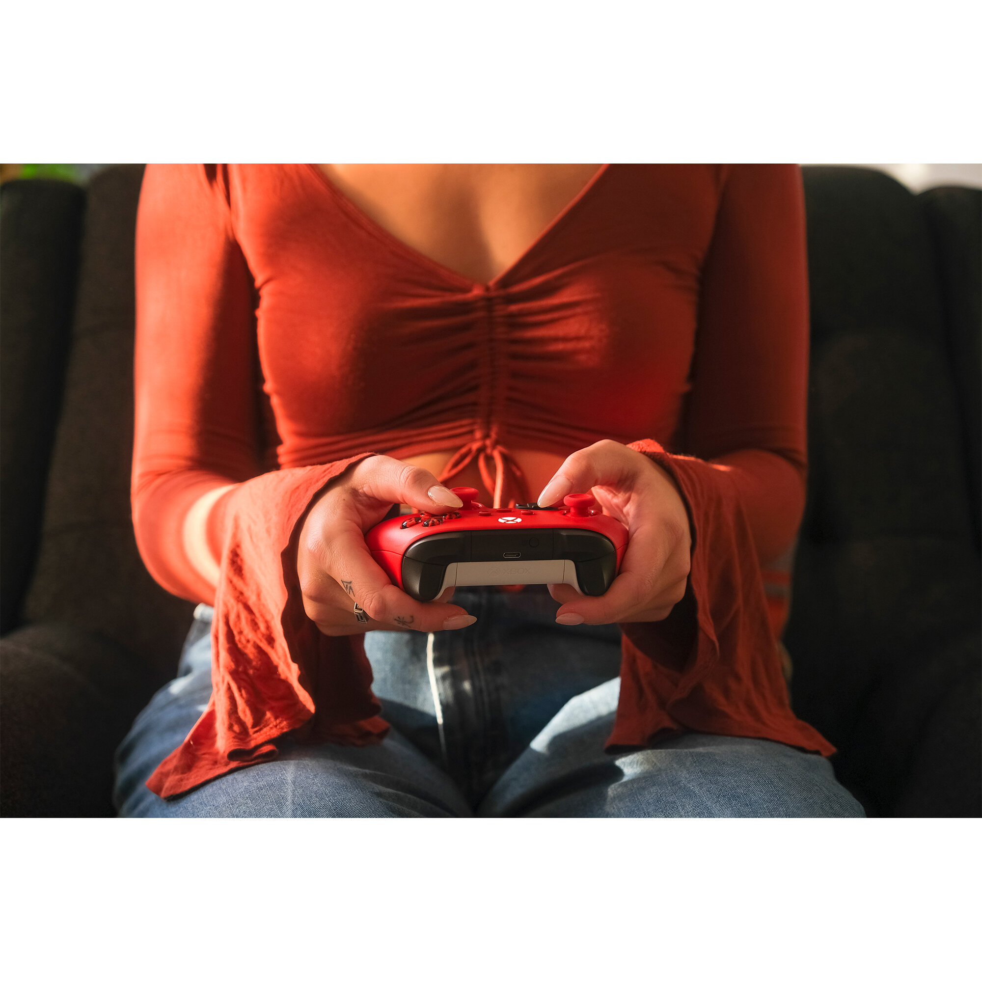 Osoba trzyma czerwony kontroler do gier. Kontroler ma czarne przyciski i jest przed telewizorem.