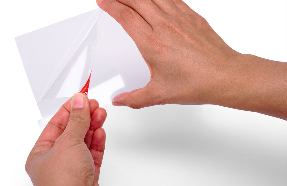 Dłonie odklejające plastikową folię. Czerwona zakładka jest ciągnięta.