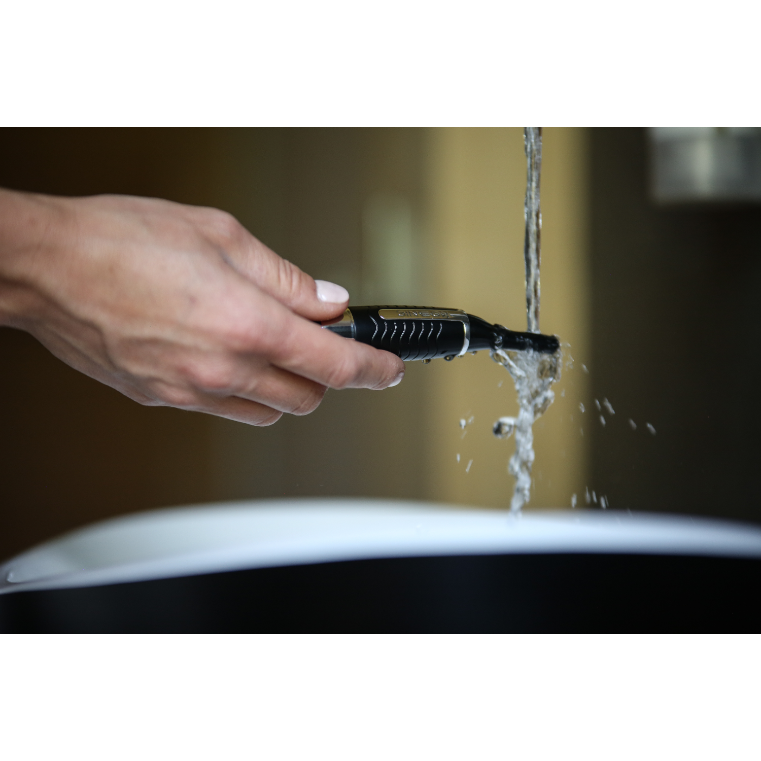Een hand die een zwarte en zilveren trimmer onder stromend water houdt.