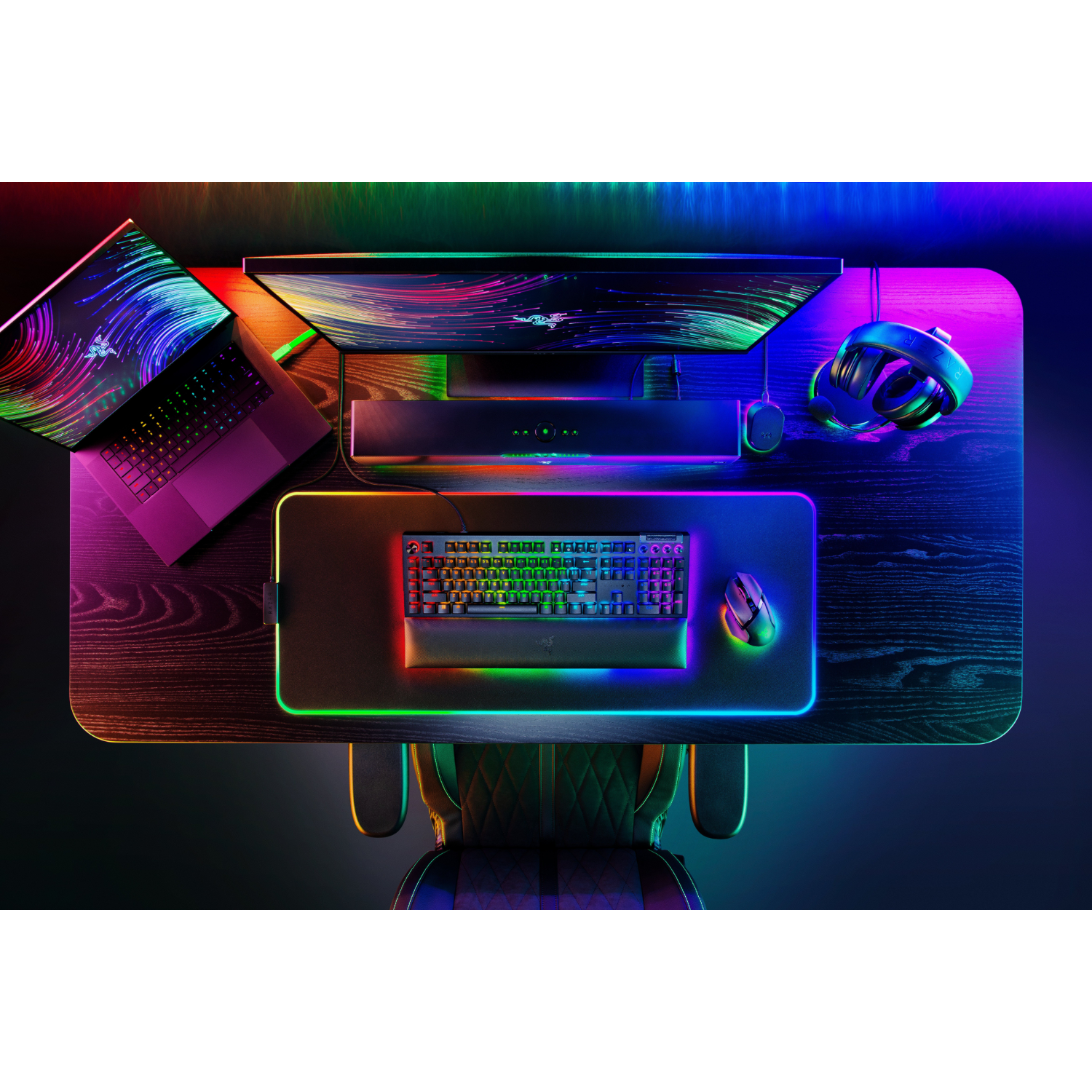 Van bovenaf gezien een gaming-opstelling met een laptop, monitor, toetsenbord en RGB-verlichting.