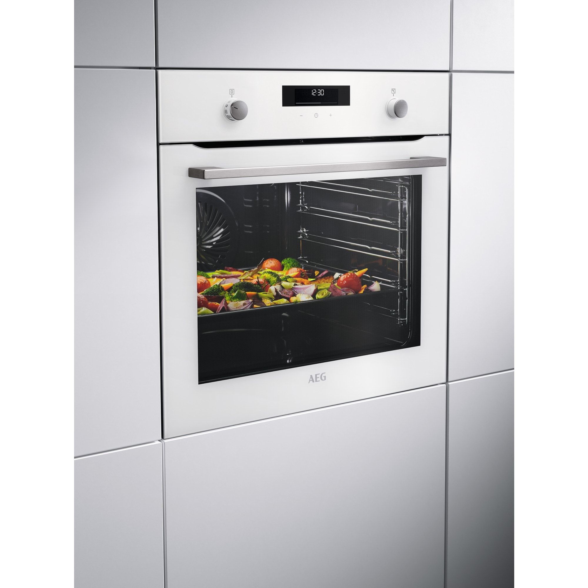 Horno blanco empotrado con verduras asadas dentro. Pantalla muestra 12:30.