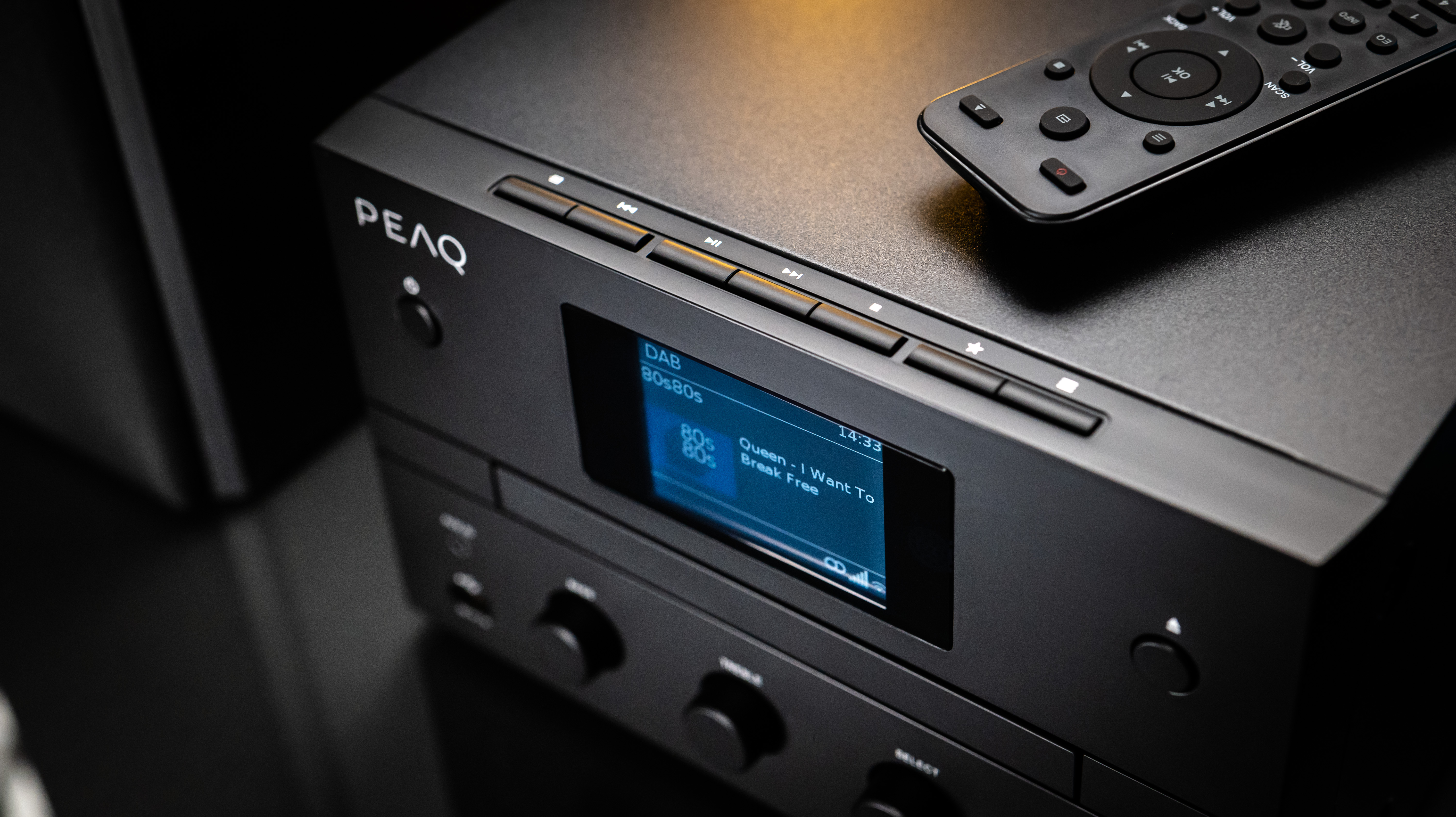 Fekete sztereó rendszer távirányítóval. A kijelzőn a lejátszott dal látható.