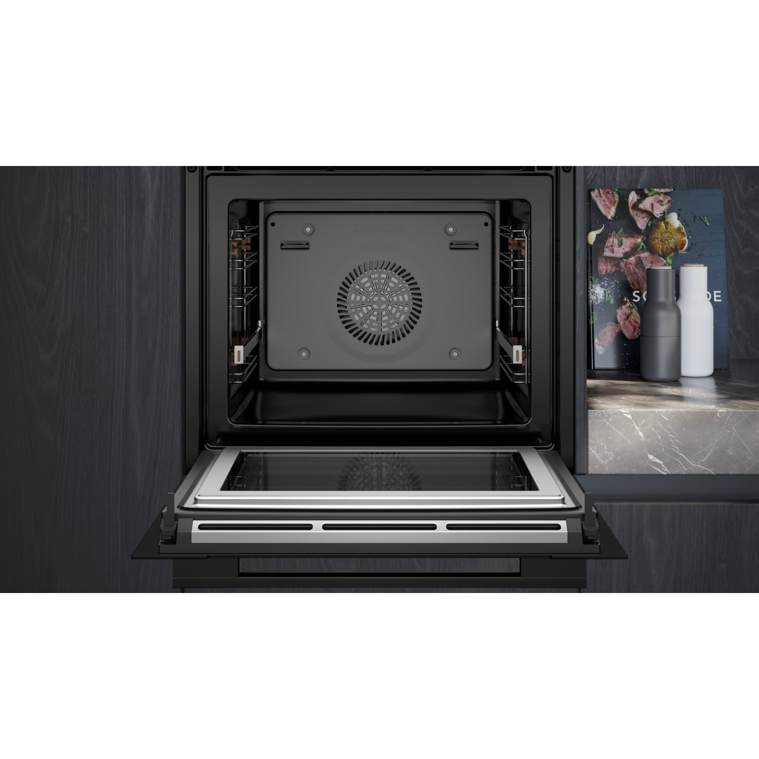 Inside a black oven, the door is open. The interior has a fan and a light. The background is dark.